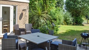 Une terrasse extérieure avec des meubles en osier, une table et un barbecue.