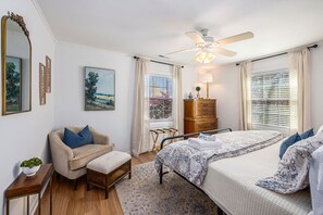A bedroom with a bed, a chair, a dresser, a window with blinds, a ceiling fan, and a painting on the wall. - Charming 3br/2ba Shem Creek Oasis! (Mount Pleasant)