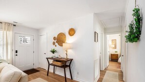 A room with a wooden floor, a white door, a small table with a lamp, and a plant. - Charming 3br/2ba Shem Creek Oasis! (Mount Pleasant)