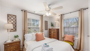 A bedroom with a bed, bedside table, lamp, decorative wall piece, and a ceiling fan. - Charming 3br/2ba Shem Creek Oasis! (Mount Pleasant)
