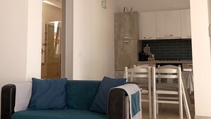 A living room with a teal sofa, a kitchen area with a black tiled backsplash, and a white ceiling with exposed beams. - Le Terrazze sul Sale - Studio Apartment 2 (Salinagrande)