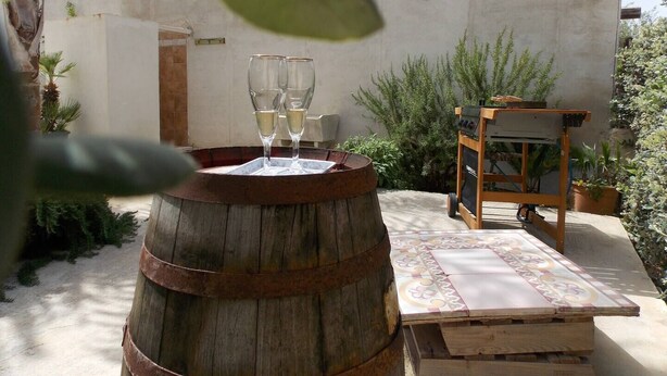 A rustic outdoor setting with a wooden barrel table, two glasses of white wine, and a wooden cart with a patterned tablecloth. - Le Terrazze sul Sale - Studio Apartment 2 (Salinagrande)