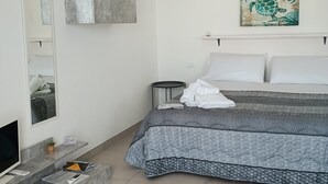 A modern bedroom with a bed, a television, a small table with a plant, and a painting on the wall. - Le Terrazze sul Sale - Studio Apartment 2 (Salinagrande)