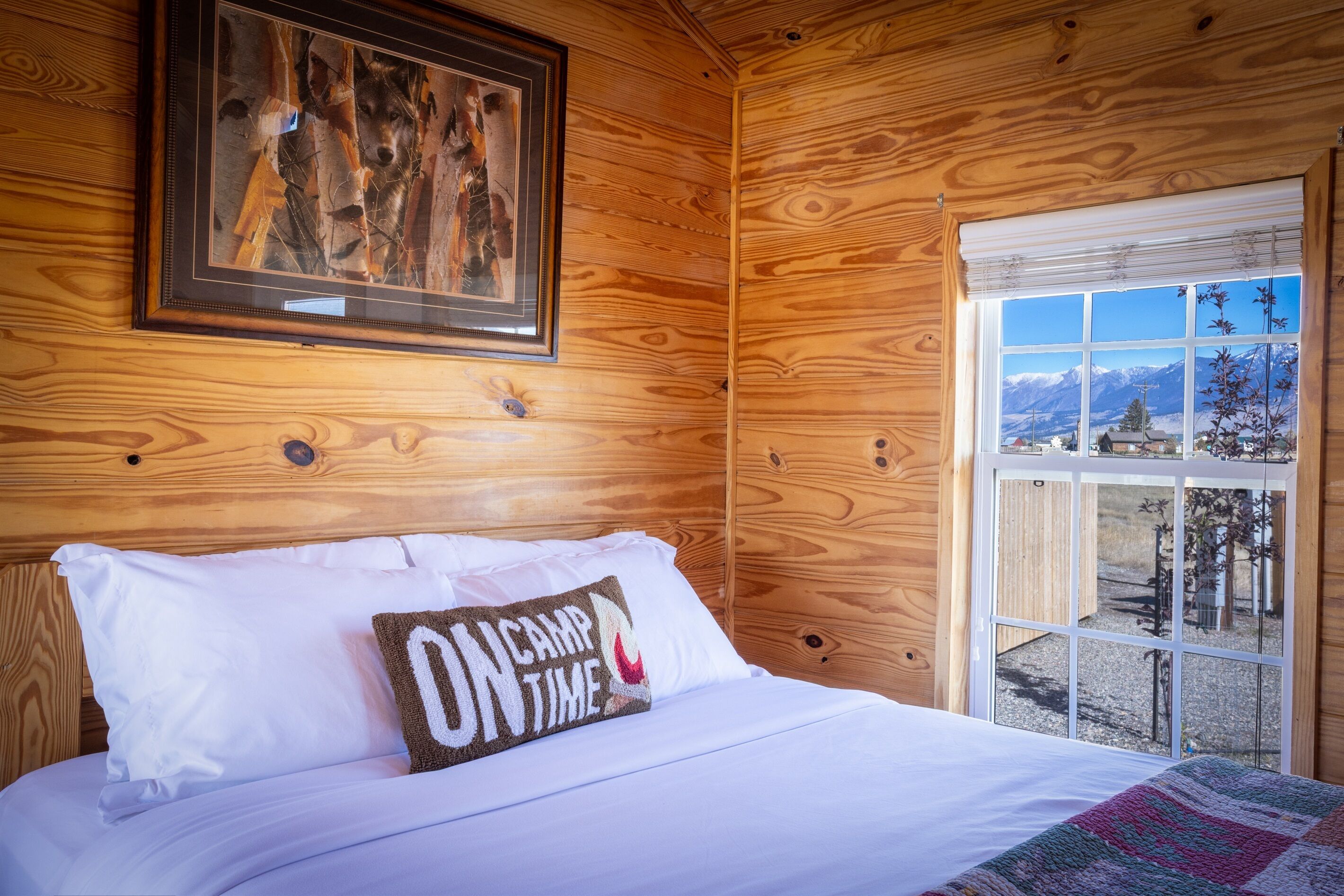 Une chambre rustique en bois, avec un lit, un tableau encadré au mur et une fenêtre donnant sur les montagnes.