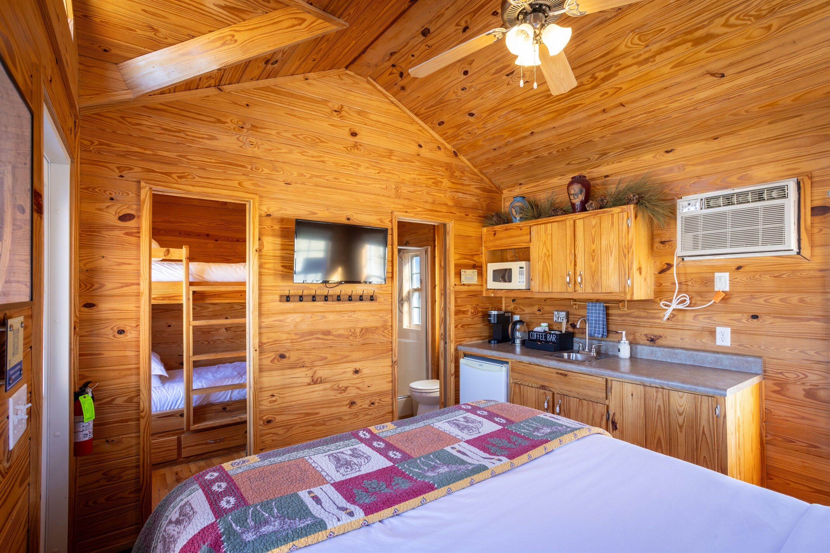 L’intérieur d’une cabane en bois comprend un lit superposé, un coin cuisine et un ventilateur de plafond.