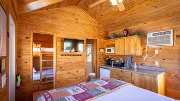 L’intérieur d’une cabane en bois comprend un lit superposé, un coin cuisine et un ventilateur de plafond.