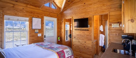 Una cabaña de madera con una cama, un televisor, un lavabo y una ventana con vistas a las montañas.