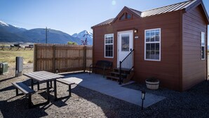 A small, single-story wooden cabin with a front porch, a bench, and a picnic table.