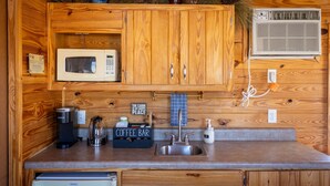 A compact kitchen with wooden cabinets, a microwave, a coffee maker, and a coffee bar sign.
