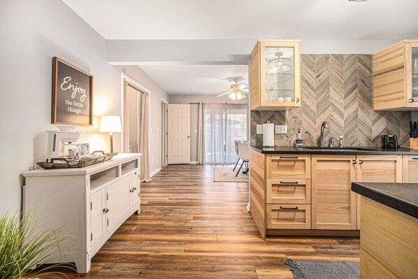 A modern kitchen with wooden cabinets, a herringbone-patterned backsplash, and a dining area with a ceiling fan.