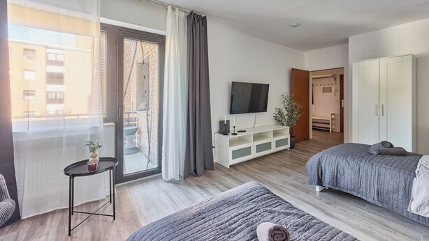 A modern hotel room with a large window, a flat-screen TV, a white wardrobe, and two beds. - Marta - Stylish Temporary Living in Bergheim (Bergheim)