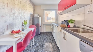 A compact kitchen with red cabinets, a white countertop, and a dining area with red chairs. - Marta - Stylish Temporary Living in Bergheim (Bergheim)
