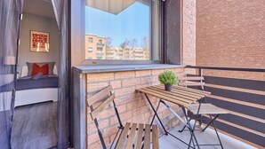A balcony with a wooden table, a potted plant, and a view of a building in the background. - Marta - Stylish Temporary Living in Bergheim (Bergheim)