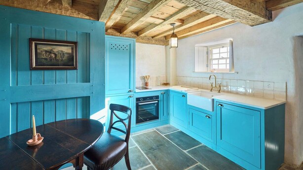 Una cocina con armarios azules, suelo de piedra y techo de madera rústica.