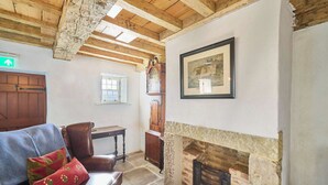 Una habitación rústica con vigas de madera a la vista, chimenea, un cuadro enmarcado, una puerta de madera y una ventana.
