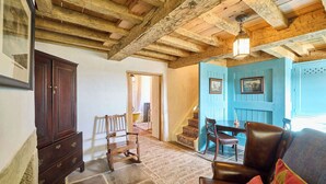 Un interior rústico con vigas de madera a la vista, una zona de comedor con paneles azules y una silla de madera tradicional.