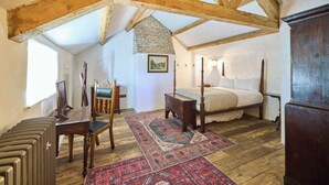 Un dormitorio con una cama con dosel, una silla de madera, un aparador y un ventanal grande.