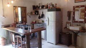 Cocina compacta con estufa, fregadero y refrigerador. Hay una mesa de madera con una silla, una planta en maceta y un espejo en la pared.