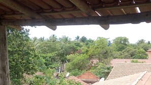 Una habitación con colcha estampada, baranda de balcón de madera y vistas a una zona residencial con tejados rojos y vegetación.