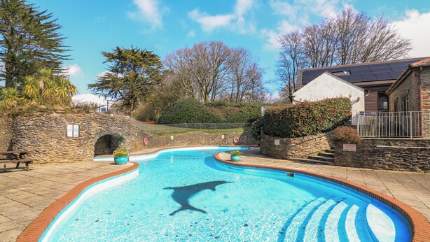 A swimming pool with a dolphin sculpture, surrounded by stone walls and a stone bench. - Millers Loft (Ivybridge)