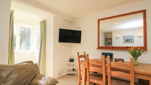 A living room with a leather sofa, wooden dining table, chairs, a flat-screen TV, a mirror, and a window with curtains. - Millers Loft (Ivybridge)