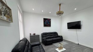 Una sala de estar moderna con un sofá de cuero negro, una mesa de centro de vidrio y un televisor montado.