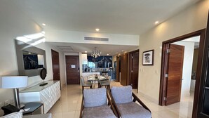 A modern living room with a dining area, a kitchen in the background, and a hallway leading to other rooms. - Gorgeous Oceanfront 2BR Cabo Rental – Ocean Views, Infinity Pool & Luxe Vibes (San José del Cabo)