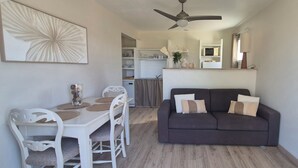 A dining area with a white table and chairs, a dark-colored sofa with cushions, and a ceiling fan. - A l'ombre du clocher - Gîte with heated pool (Calenzana)