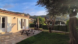 A house with a stone patio, a wooden table, and a barbecue grill. - A l'ombre du clocher - Gîte with heated pool (Calenzana)