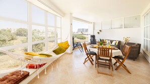 A bright, open-plan living space with a dining area, a hammock, and a view of the city.