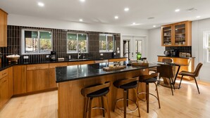 A modern kitchen with a central island, wooden cabinets, and a bar area with stools. - Private Fairhope Waterfront Retreat, Two Complete Residences, Sleeps Up to 14 (Fairhope)