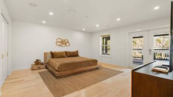 A bedroom with a bed, a desk, a window, and a door.