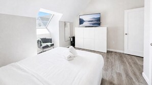 Ein modernes Hotelzimmer mit einem großen Bett, einem Fernseher auf einer Kommode und einem Blick ins Freie durch ein Oberlicht.