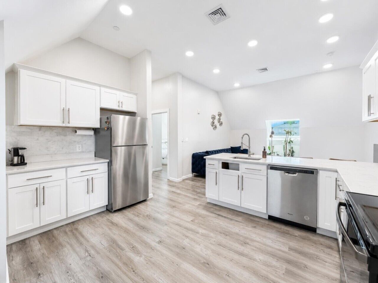 A modern kitchen with white cabinetry, stainless steel appliances, and a wooden floor.