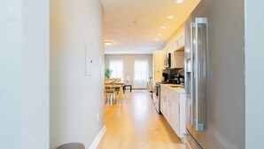 A modern kitchen with stainless steel appliances, wooden flooring, and a dining area with a table and chairs.
