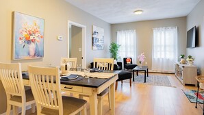 A dining area with a table set for four, a mirror, and a painting of flowers.