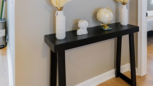 A console table with a globe, two vases with dried flowers, and a mirror.