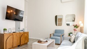 A modern living room with a wooden cabinet, a grey sofa, a blue armchair, and a flat-screen TV mounted on the wall. - Stylish Wooster Square Home Walk to Yale (New Haven)