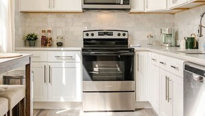 A modern kitchen with white cabinets, a stainless steel oven, a microwave, and a coffee maker. - Stylish Wooster Square Home Walk to Yale (New Haven)