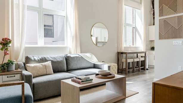 A modern living room with a grey sofa, a wooden coffee table, and a dining area with a white table and chairs. - Stylish Wooster Square Home Walk to Yale (New Haven)