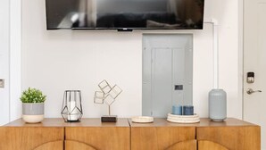 A wooden console table with a flat-screen TV mounted above it, a potted plant, a geometric glass sculpture, and a vase. - Stylish Wooster Square Home Walk to Yale (New Haven)