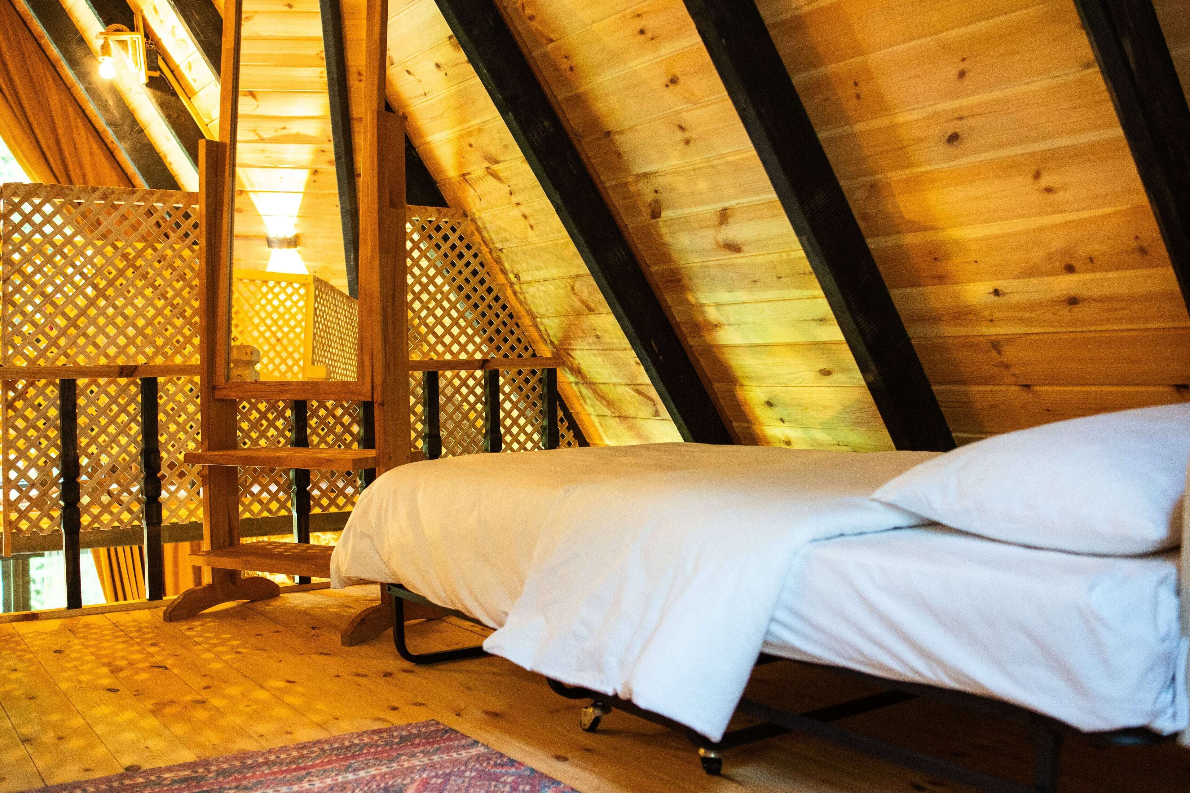 Une chambre mansardée en bois, avec un lit, une échelle en bois et une cloison ajourée.