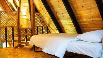 Une chambre mansardée en bois, avec un lit, une échelle en bois et une cloison ajourée.