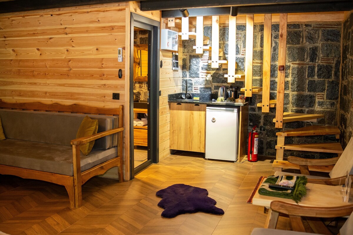 Een gezellig houten blokhutinterieur met een houten bank, een kleine keukenhoek en een stenen muur.
