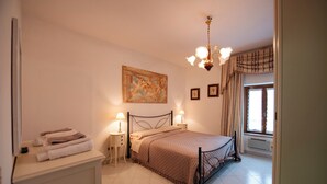 Quarto com cama, abajures, um quadro na parede e janela com cortinas.