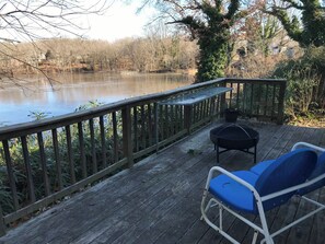 A wooden deck with a view of a lake, a grill, and a blue chair.
