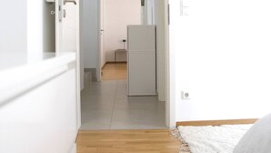 A narrow hallway with a wooden floor leading to a kitchen area.