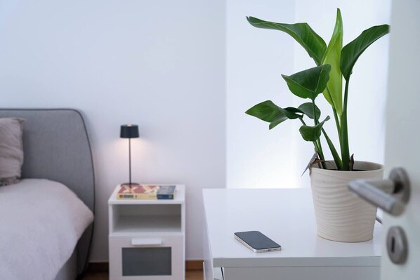 Un dormitorio minimalista con cama, mesita de noche, lámpara y una planta en maceta.