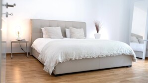 A modern bedroom with a large bed, a bedside table with a lamp, and a potted plant.