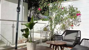 An outdoor patio with a table and chairs, a potted plant, and a white wall with climbing plants.